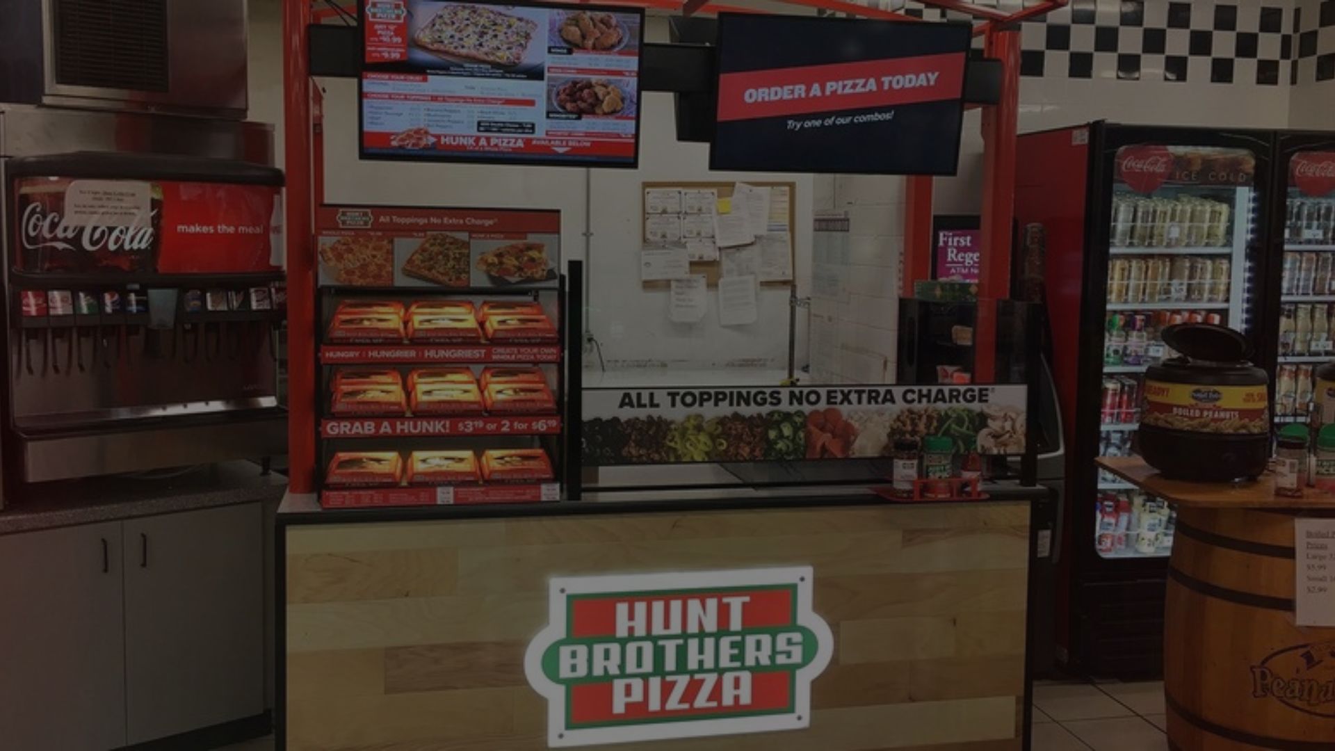 Untitled design 8 - TapTapEat Pizza shop counter with digital menu boards and a large 'Order a Pizza Today' sign above, promotional pizza toppings display in front, and Hut Brothers Pizza logo on the front of the counter.